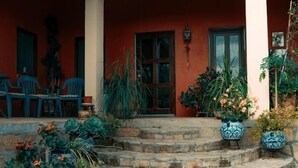 A stone staircase leading to a covered porch with a red wall, potted plants, and outdoor seating. - CASONA DOS VIDAS (Tequisquiapan)