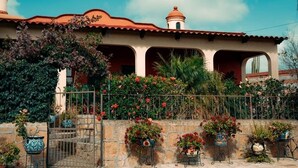 A building with a red-tiled roof, a bell tower, and a stone wall with potted plants. - CASONA DOS VIDAS (Tequisquiapan)
