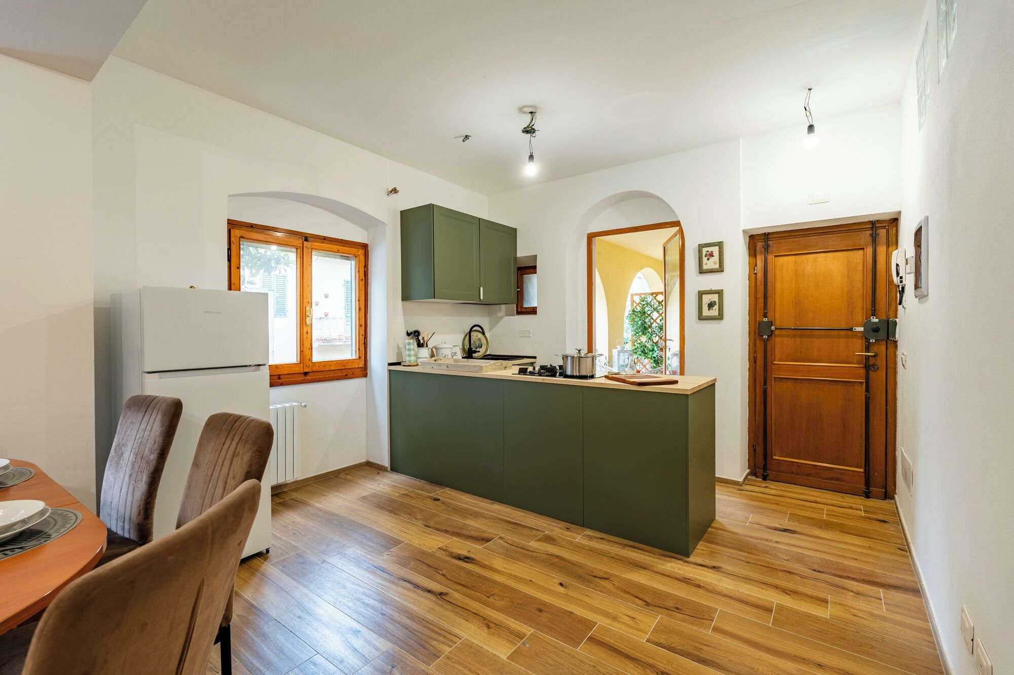 A compact kitchen with a central island, wooden flooring, and a dining area with chairs.