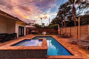 A rectangular swimming pool with a brick border, surrounded by lounge chairs and a dining area with chairs and a table. - Lux/Heated Pool/Jacuzzi/Firepit/Games/1mile to beach (Naples)