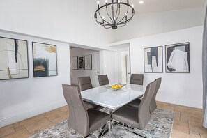 A modern dining room with a white table, six gray chairs, and a chandelier. - Lux/Heated Pool/Jacuzzi/Firepit/Games/1mile to beach (Naples)