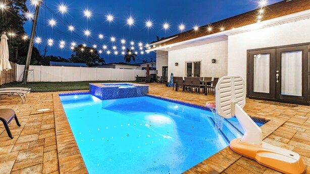 Una piscina con bordo piastrellato, una vasca idromassaggio e luci a stringa.