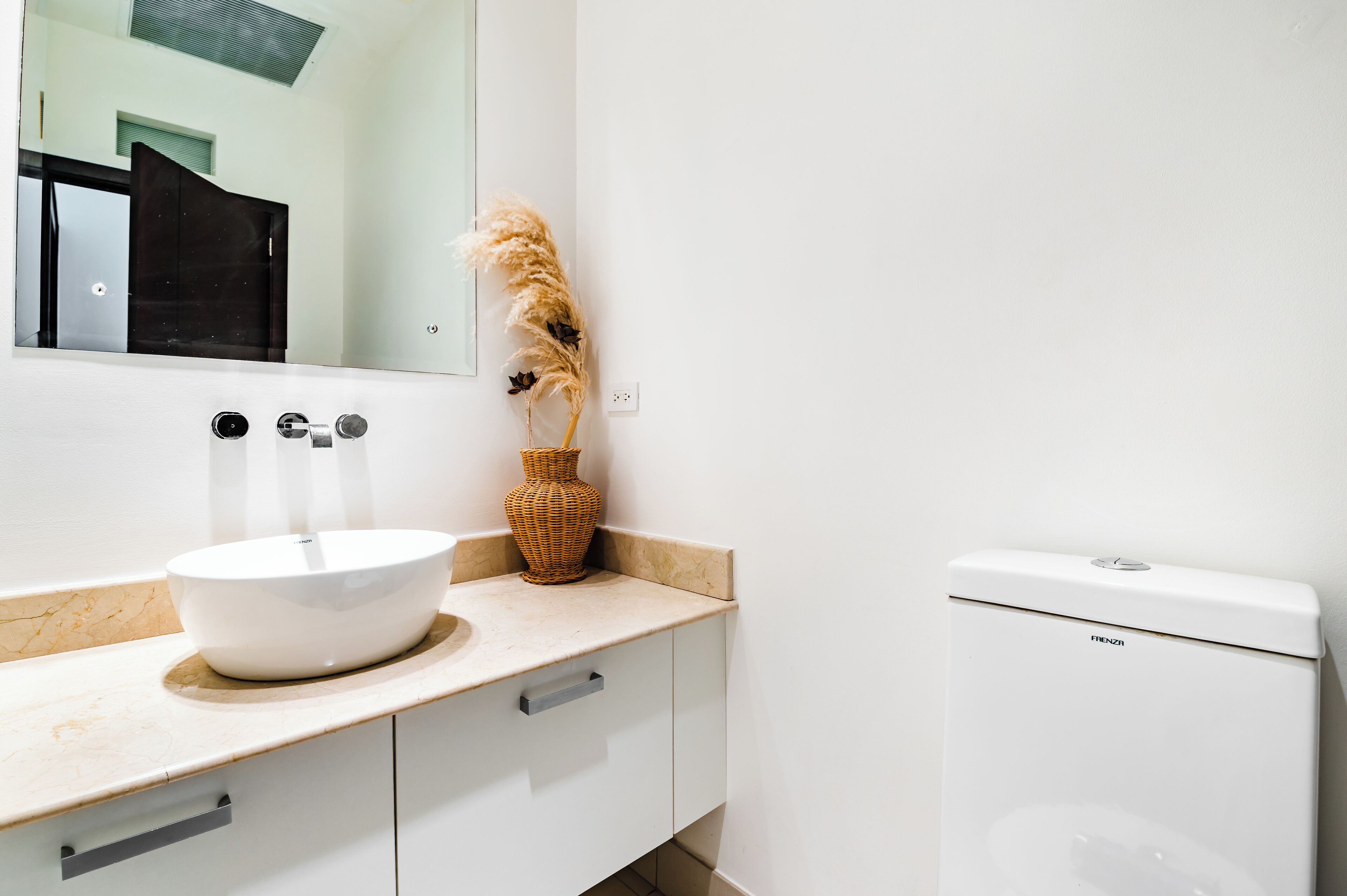 A bathroom with a white sink, a mirror, a toilet, and a decorative vase with pampas grass.