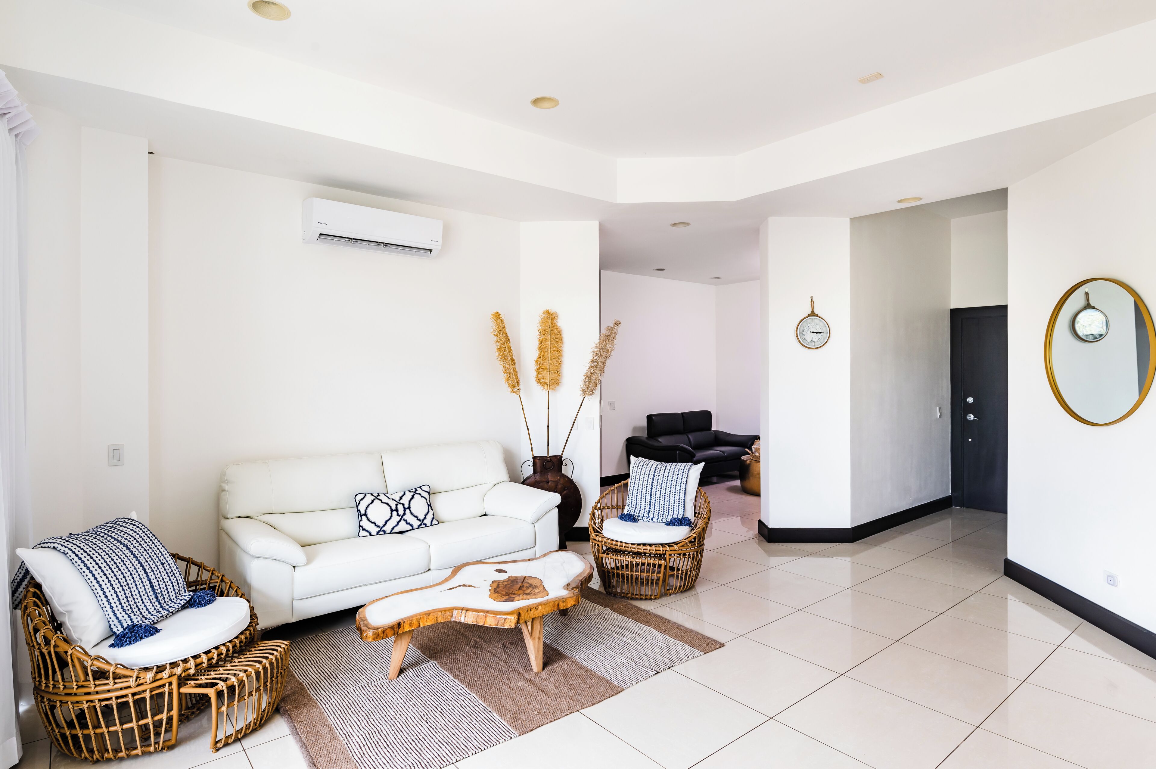 Una sala de estar moderna con un sofá blanco, sillas de mimbre, una mesita de centro y plantas decorativas.