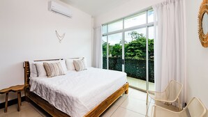 Une chambre à coucher avec un grand lit, un banc en bois, une chaise et une vue sur la verdure par une grande fenêtre.