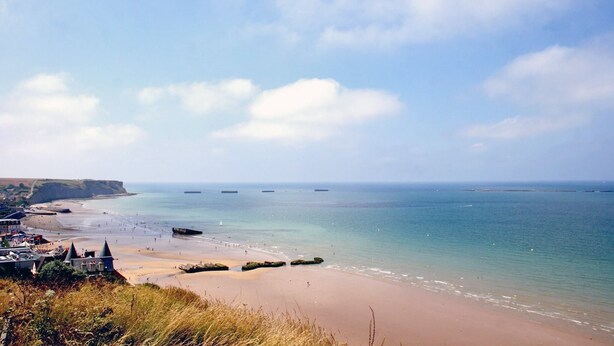A coastal view with a beach, cliffs, and a distant ship.