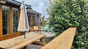 An outdoor patio area with wooden tables and chairs, a large umbrella, and a stone wall.