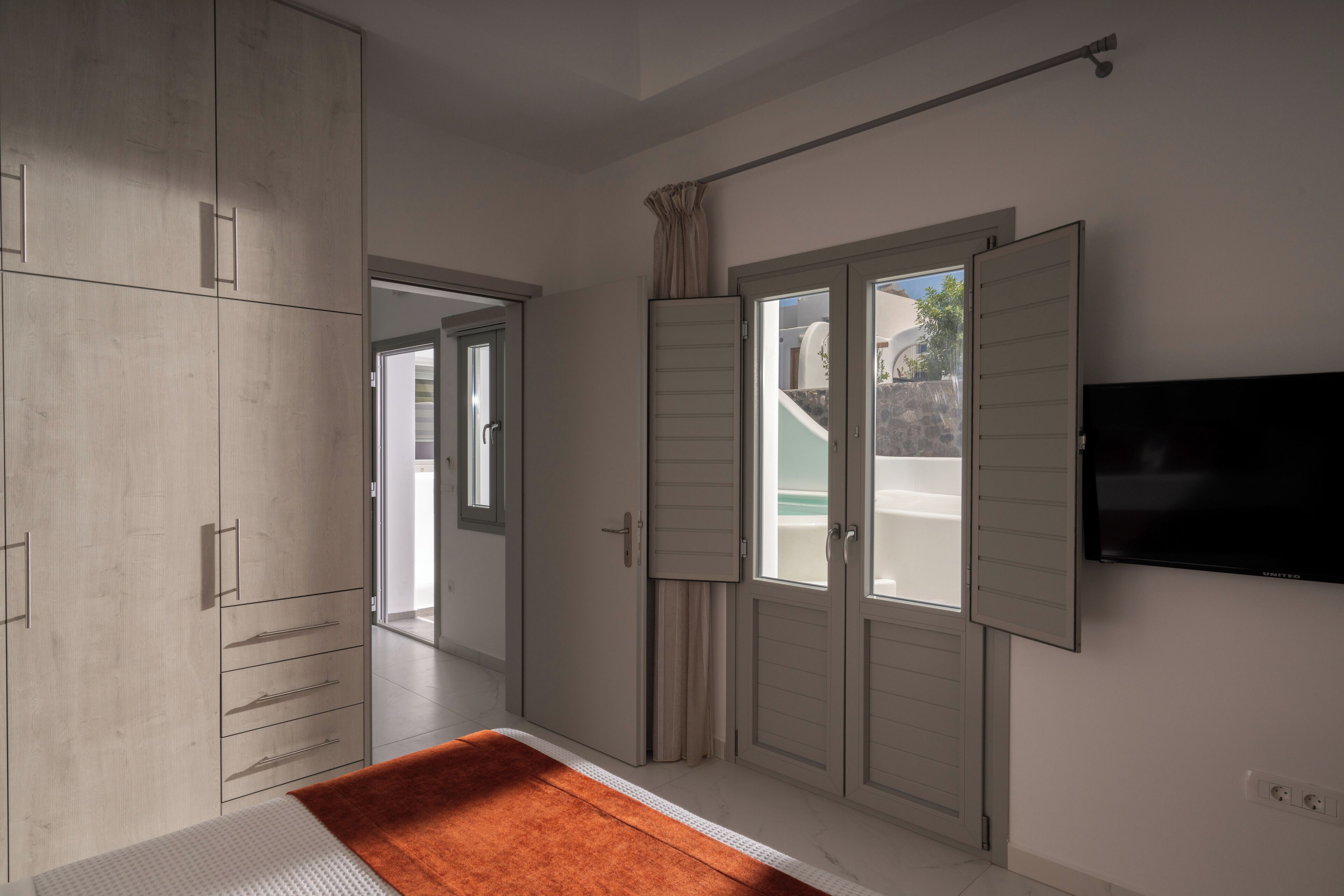 Een slaapkamer met een bed, kledingkast, schuifdeuren en een televisie.