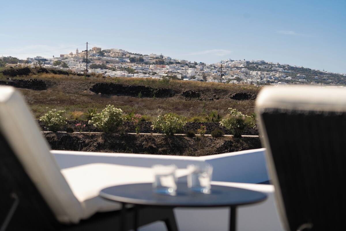 Una terraza con mesa y sillas, con vistas a un pueblo en la ladera, con edificios y una iglesia destacada.