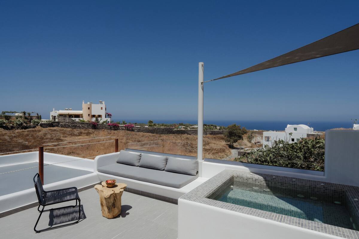 Una terraza en la azotea con una piscina infinita blanca, un sofá gris y una silla negra.