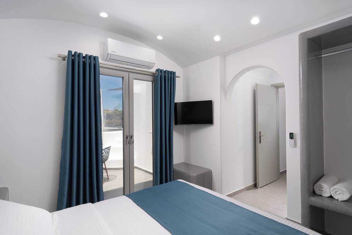 Habitación de hotel moderna con cama, televisor, equipo de aire acondicionado, balcón con una silla y zona de ducha.