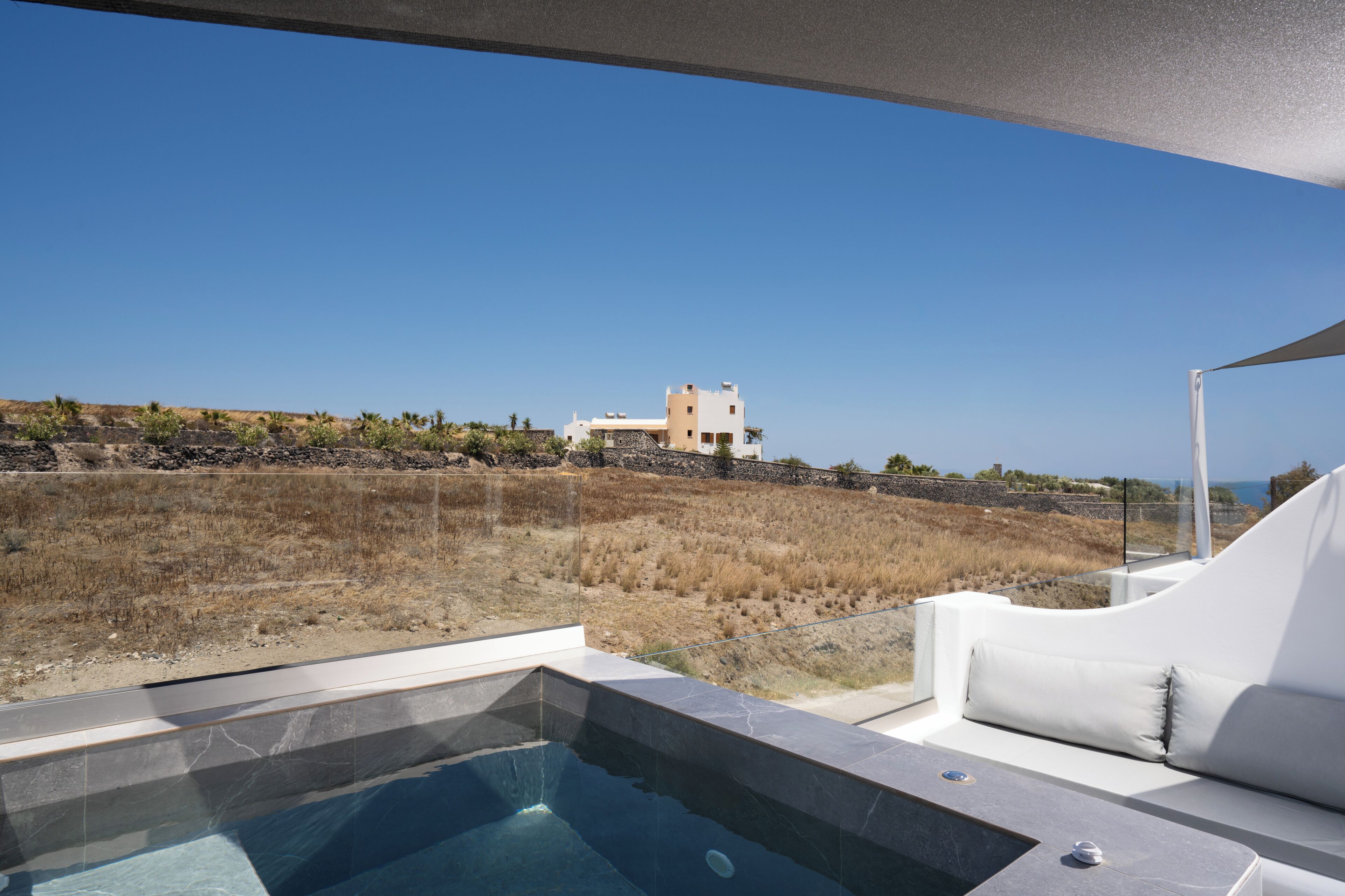 A modern outdoor pool area with a clear view of a coastal landscape and a building in the distance.
