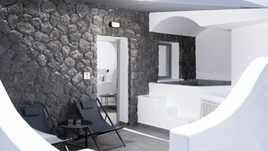A modern outdoor seating area with stone walls, a white door, and a small table with chairs. - Griseo Villas (Santorini)