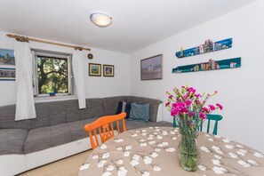 Un salon chaleureux avec un canapé gris, une table ronde recouverte d’une nappe à motifs floraux et un vase rempli de fleurs roses.