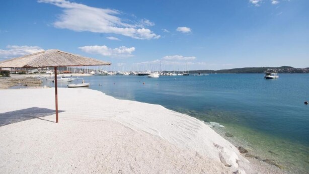 Una platja amb un para-sol de palla, embarcacions i aigua cristal·lina.