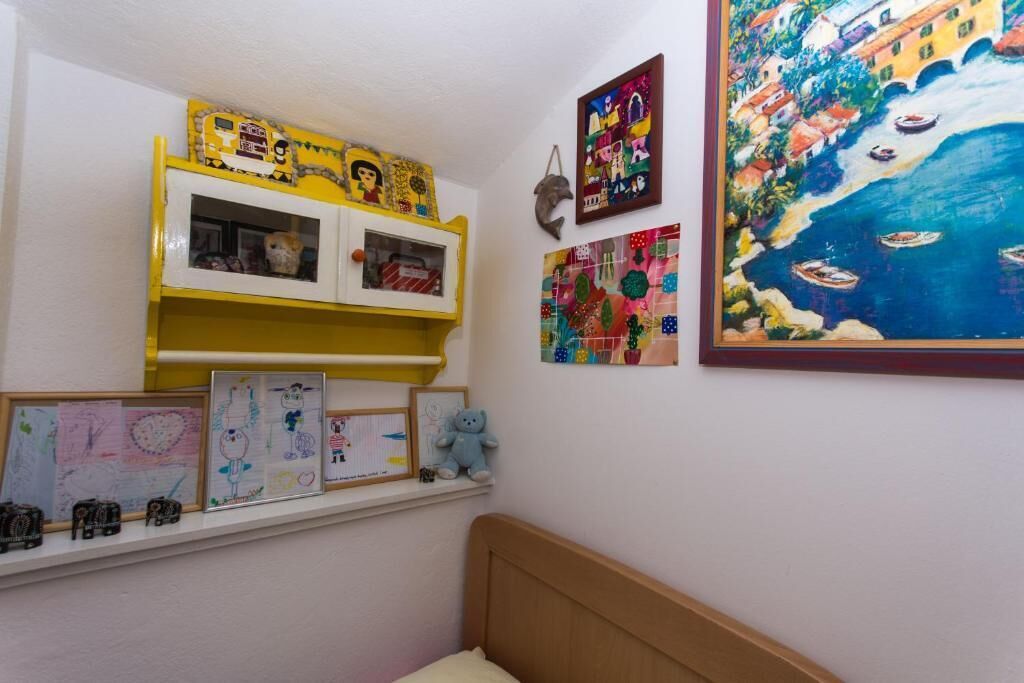 A child's room with a bed, shelves with drawings, and a large painting of a coastal scene.