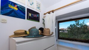 Habitació amb finestra que donava a zones verds, un taulell blanc amb gorres i decoració mural que inclou un vaixell i una corda de roba.