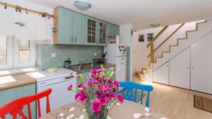 Cuina amb armaris verds blaus, un refrigerador blanc i una zona de menjador amb taula i cadires.