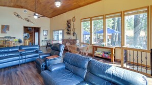 A spacious living room with a wooden ceiling, leather sofas, a dining area with a table and chairs, and large windows offering a view of the outdoors. - Lakefront Bliss: Coeur d'Alene Cabin w/ Dock! (Coeur d'Alene)