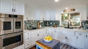 A modern kitchen with white cabinetry, stainless steel appliances, a bowl of lemons on the counter, and a window with a view of the outdoors. - Lakefront Bliss: Coeur d'Alene Cabin w/ Dock! (Coeur d'Alene)