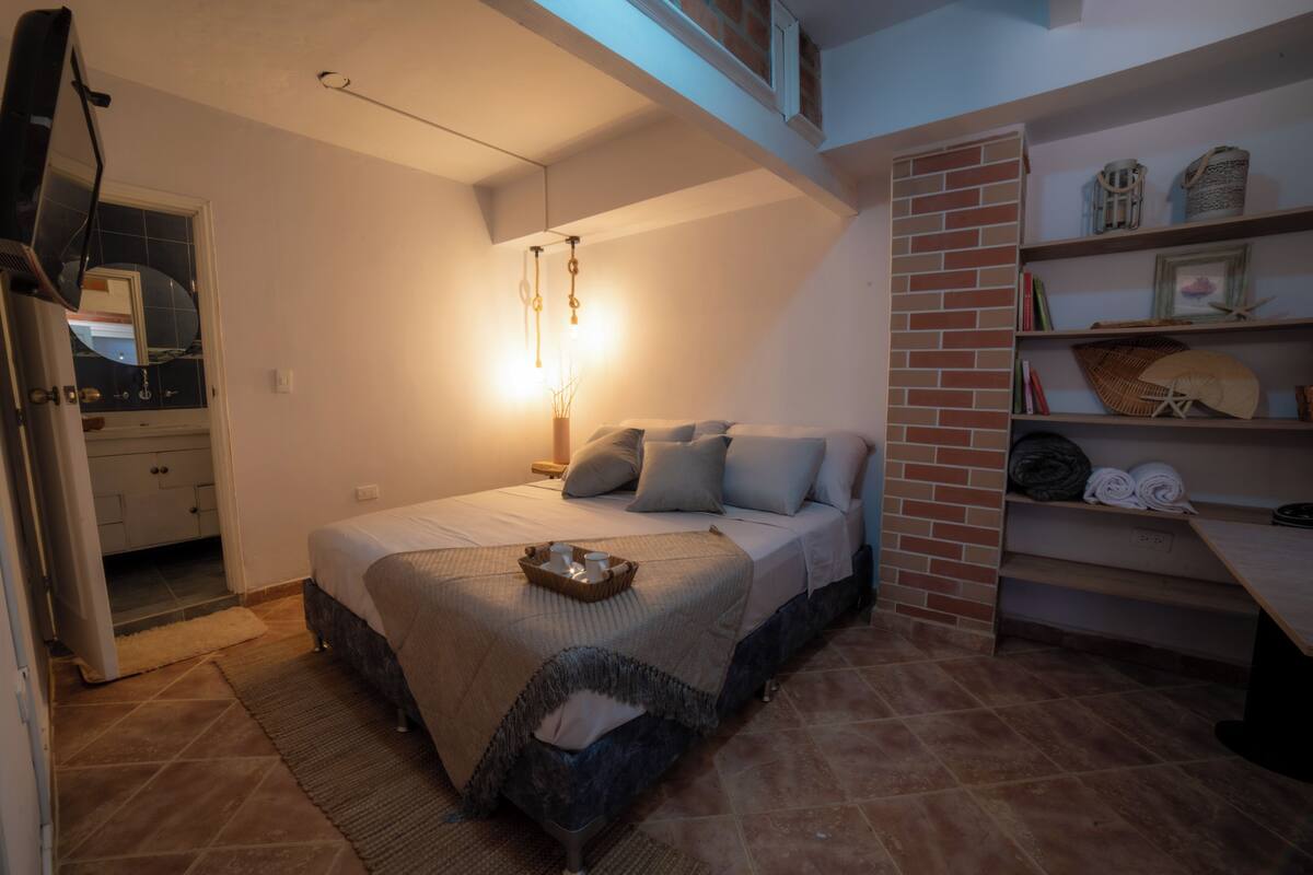 A bedroom with a bed, bedside table, and a shelf with decorative items.