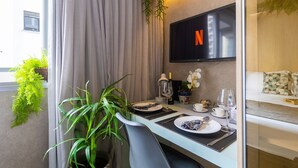 Zona pranzo con tavolo apparecchiato per due, televisore a parete e una pianta in vaso.