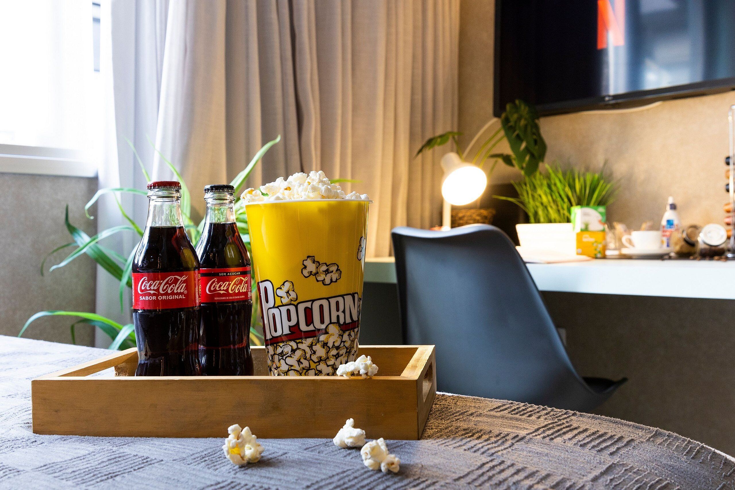 A tray with two Coca-Cola bottles, a yellow popcorn container, and scattered popcorn on a textured tablecloth.