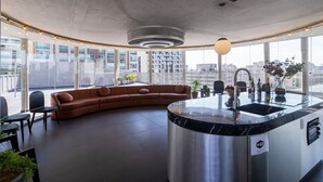 Una cucina moderna con un'isola a forma di curva, lavello integrato e vista sulla città attraverso ampie finestre.