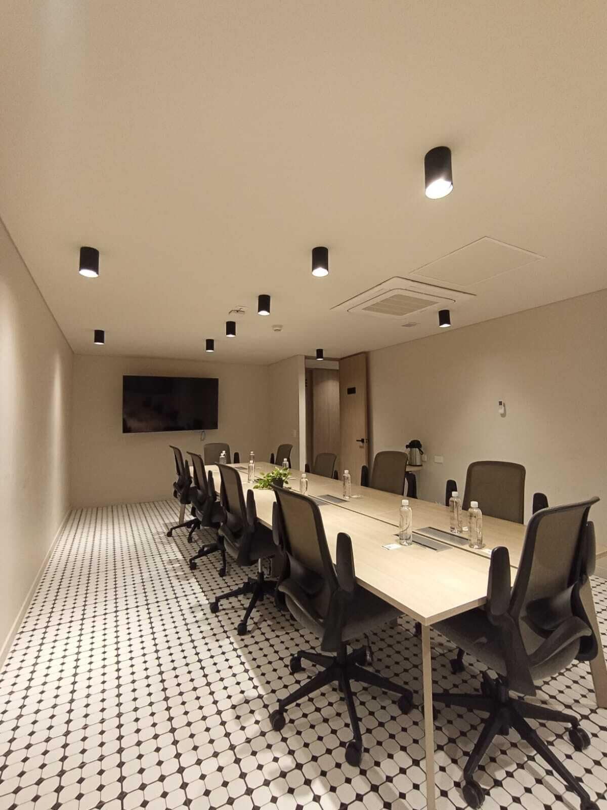 Une salle de conférence avec une longue table, de nombreuses chaises et un téléviseur à écran plat fixé au mur.