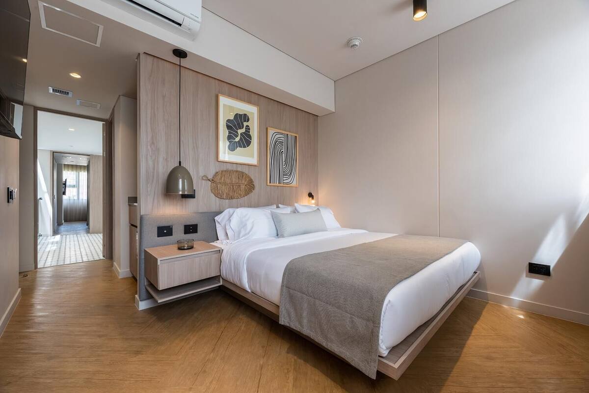 Ein modernes Schlafzimmer mit einem großen Bett, Nachttischen, einer Wandlampe und zwei gerahmten Kunstwerken.