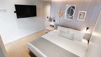 Une chambre moderne avec un grand lit, un téléviseur fixé au mur et des œuvres d’art accrochées au mur.