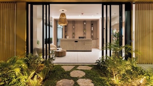 A modern reception area with a wooden reception desk, a hanging light fixture, and a glass door leading to a reception desk. - Nakúa Stay + Work (Medellín)
