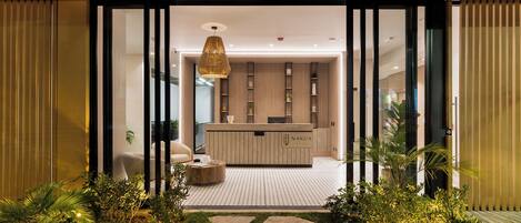 A modern reception area with a wooden reception desk, a hanging light fixture, and a glass door leading to a reception desk.