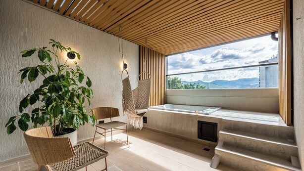 A modern spa room with a large window, a bathtub, and two wicker chairs. - Nakúa Stay + Work (Medellín)