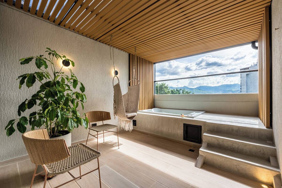 Ein moderner Wellnessraum mit großem Fenster, einer Badewanne und zwei Korbsesseln.