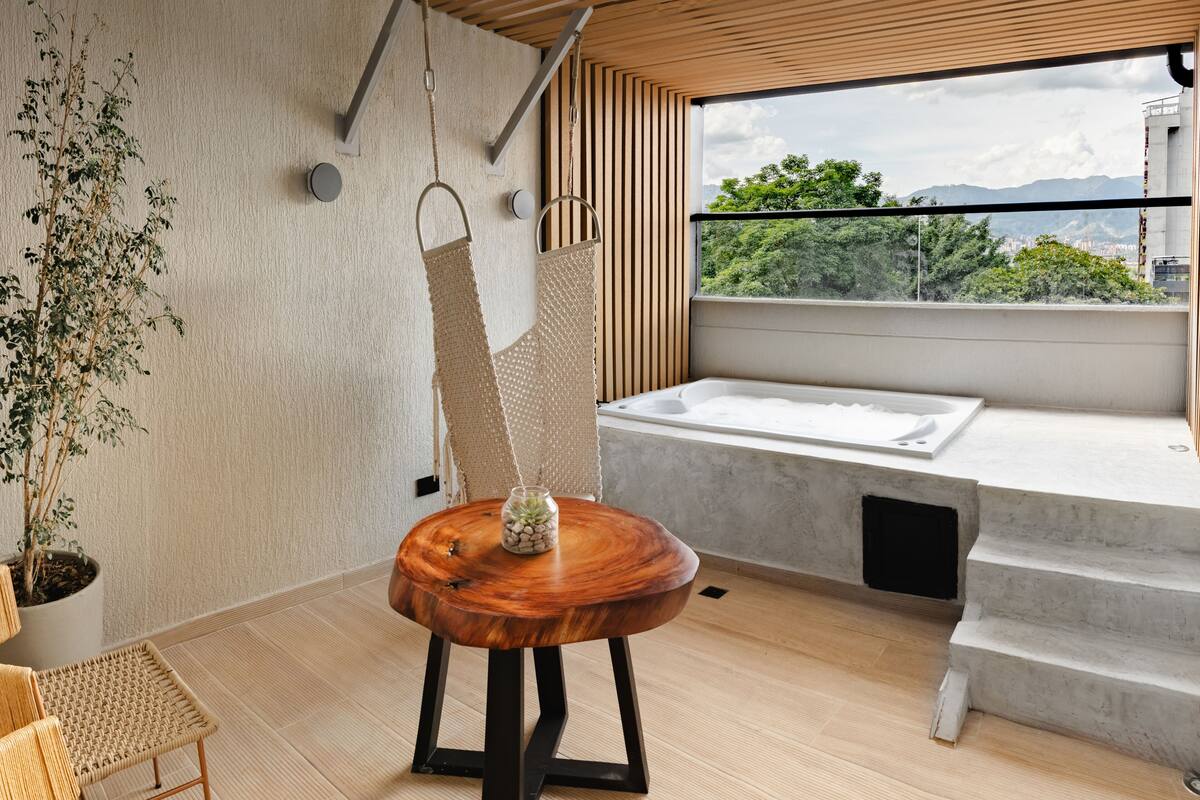Ein modernes Badezimmer mit Holzboden, einem großen Fenster mit Blick auf die Stadt, einer Badewanne und einem hängenden Handtuchhalter.