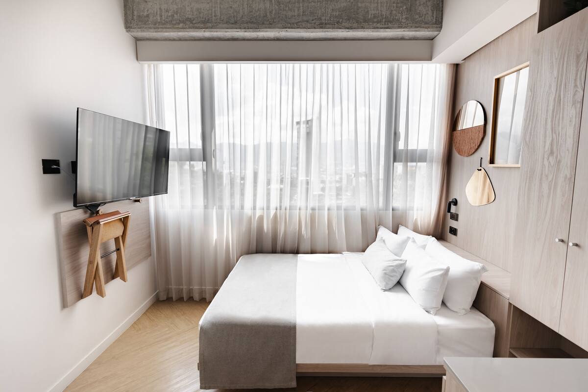 Ein modernes Hotelzimmer mit einem großen Bett, einem Flachbildfernseher, einem Nachttisch aus Holz und einem Kleiderschrank.