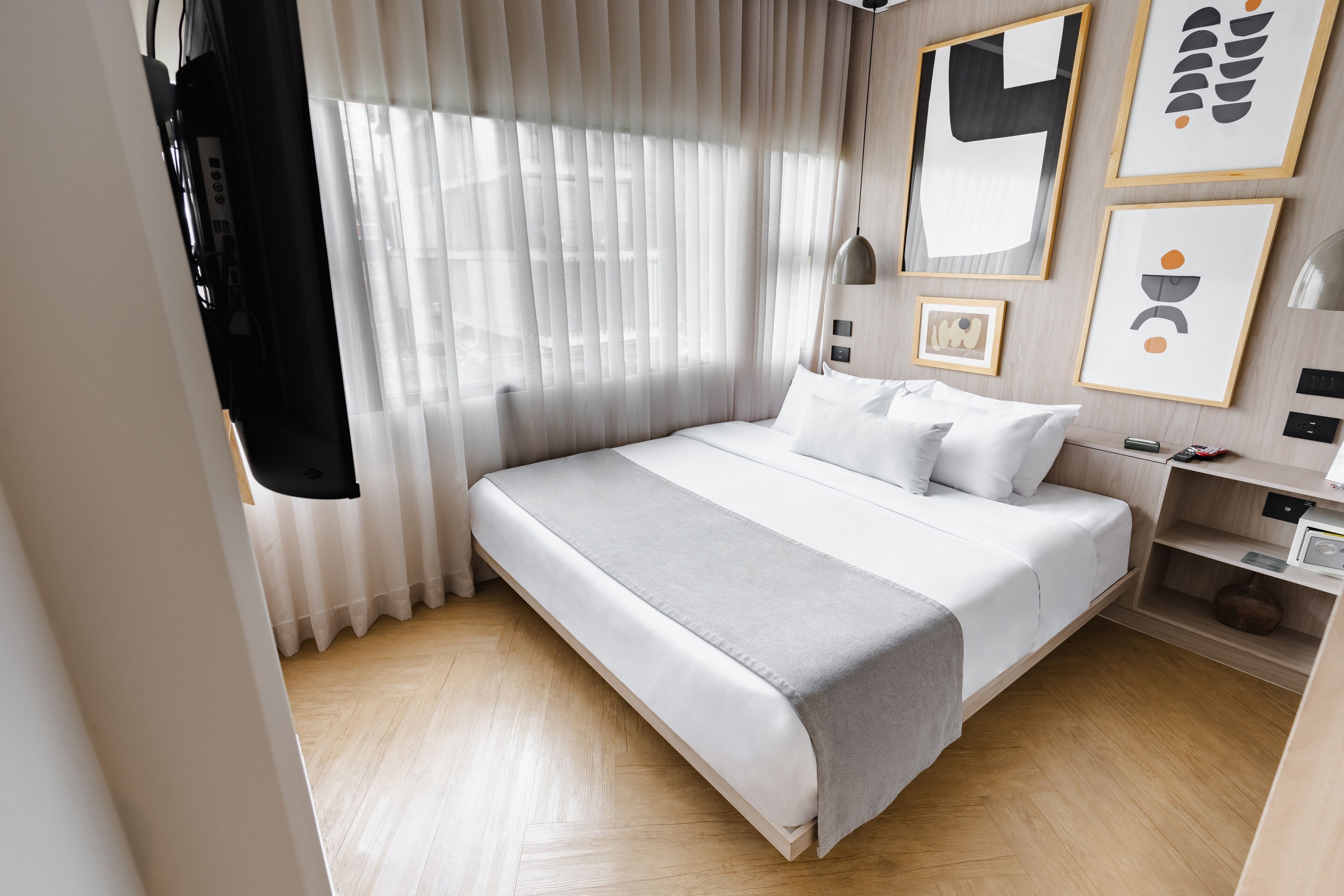 A modern hotel room with a large bed, a bedside table, a nightstand, and a wall-mounted TV.