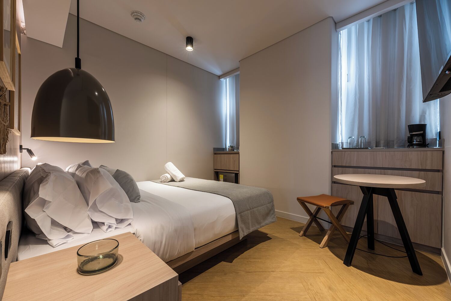 A modern hotel room with a bed, bedside table, a small round table, a sofa, and a TV.