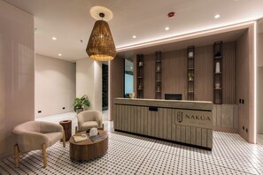 A modern reception area with a wooden reception desk, a seating area with two chairs, and a patterned floor. - Nakúa Stay + Work (Medellín)