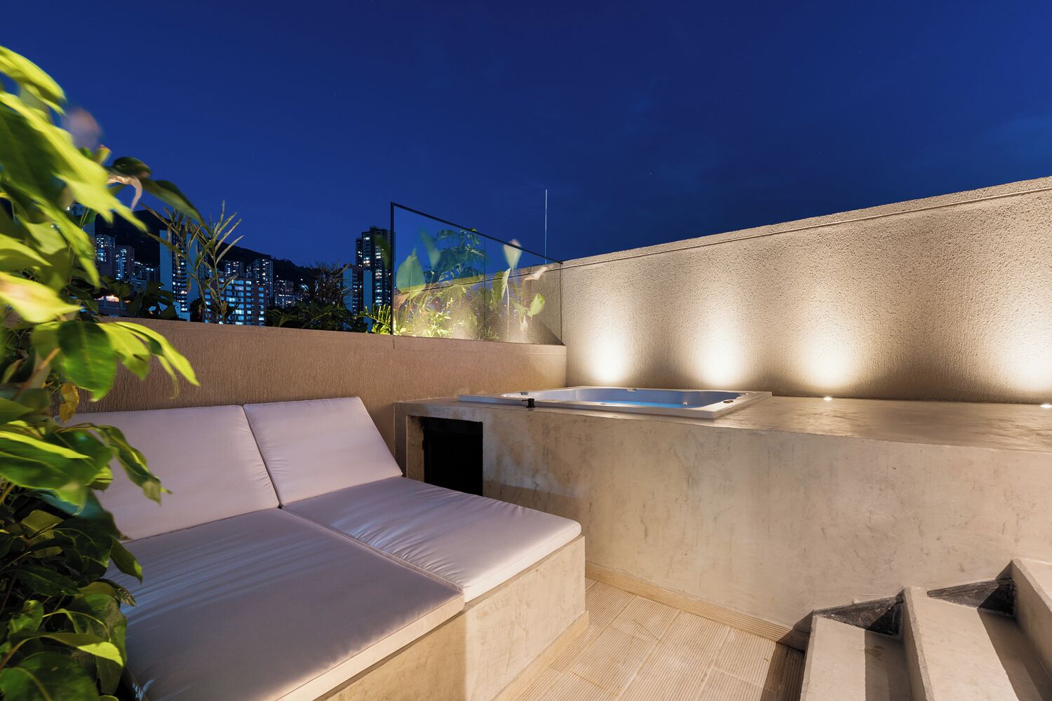 A rooftop terrace with a seating area, a hot tub, and a city view at dusk.