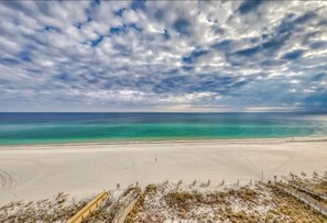 A beach with a wooden boardwalk leading to the shore, clear turquoise water, and a cloudy sky.