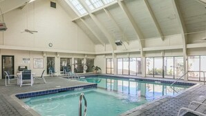 An indoor swimming pool with tiled walls, a ceiling fan, and a clock.