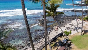A beach with rocky terrain, palm trees, and a clear view of the ocean. - Oceanfront, remodeled penthouse, sunsets, whales/dolphins, surfers! Free parking (Kailua-Kona)