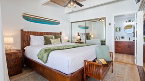 A spacious bedroom with a large bed, wooden headboard, and a ceiling fan. - Oceanfront, remodeled penthouse, sunsets, whales/dolphins, surfers! Free parking (Kailua-Kona)