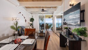 A modern living room with a dining area, a ceiling fan, and a large painting of a beach scene. - Oceanfront, remodeled penthouse, sunsets, whales/dolphins, surfers! Free parking (Kailua-Kona)