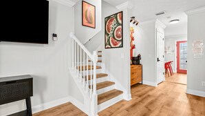 Un escalier avec des rampes blanches et des marches en bois menant à un coin repas où se trouvent une chaise rouge et une table en bois.