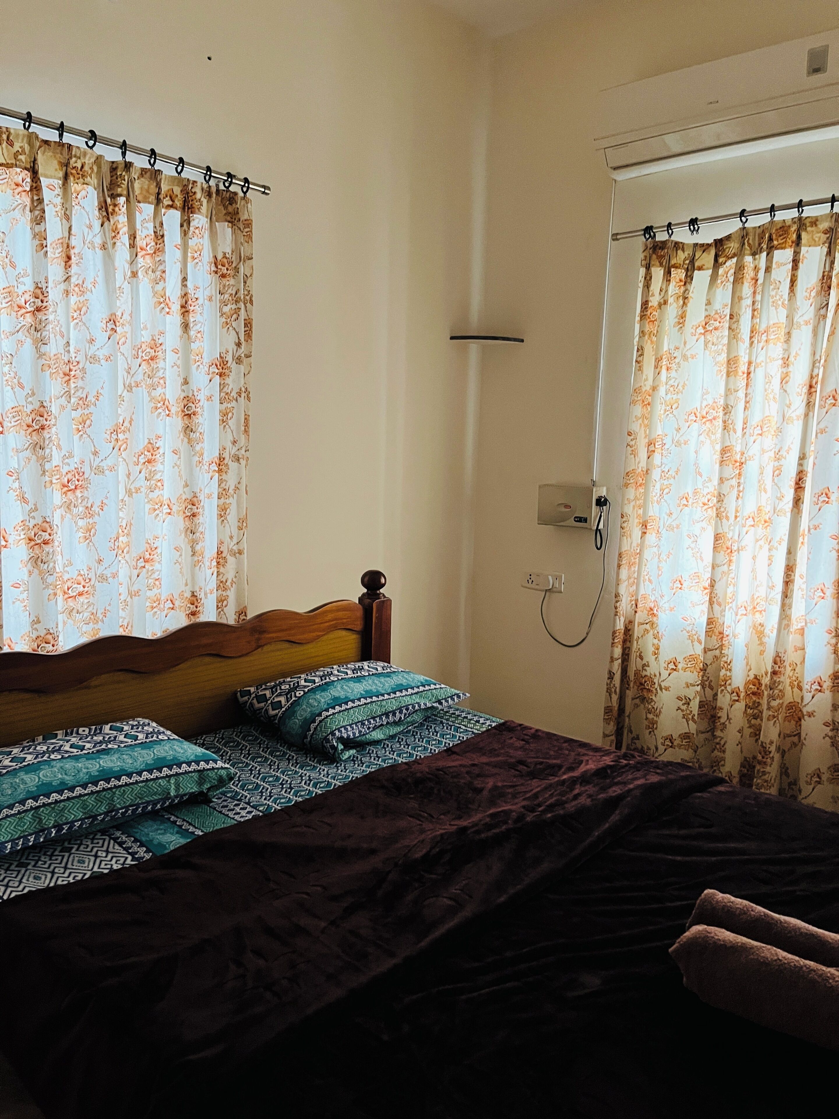 Een slaapkamer met een bed, bloemen gordijnen, een douche en een stopcontact aan de muur.