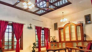 Una habitación amplia con techo alto, ventanas grandes con cortinas rojas, un armario de madera y una silla de madera.