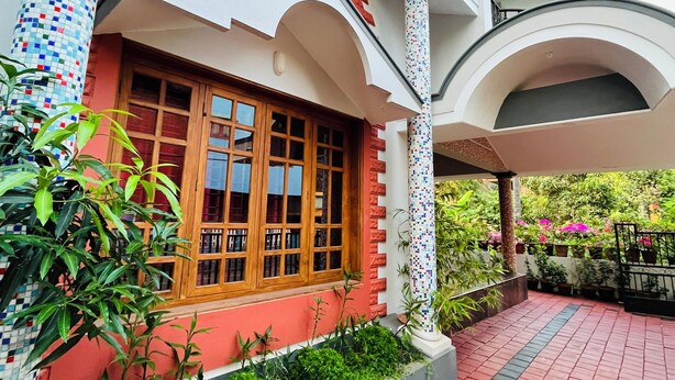 Un edificio con fachada roja y blanca, una entrada con azulejos y un balcón con plantas.